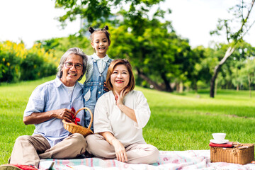 Portrait of happy love asian grandfather with grandmother and asian little cute girl enjoy relax in summer park.Young girl with their laughing grandparents smiling together.Family and togetherness