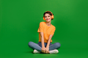 Full length photo of charming peaceful girl sit floor enjoy new playlist isolated on green color...