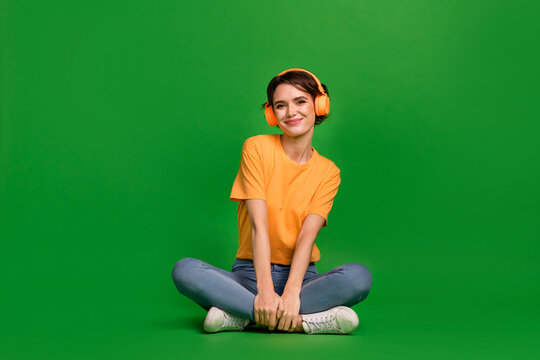 Full length photo of charming peaceful girl sit floor enjoy new playlist isolated on green color background