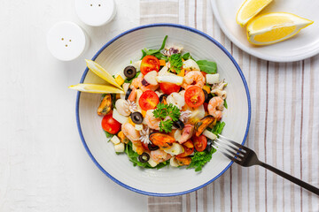 Top view of Italian mixed seafood salad. Insalata di mare. Calamari, shrimp, clams, tomatoes, bell pepper, parsley and olives. White table surface..