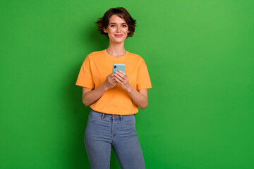Photo of sweet shiny young woman dressed orange t-shirt typing modern device empty space isolated green color background