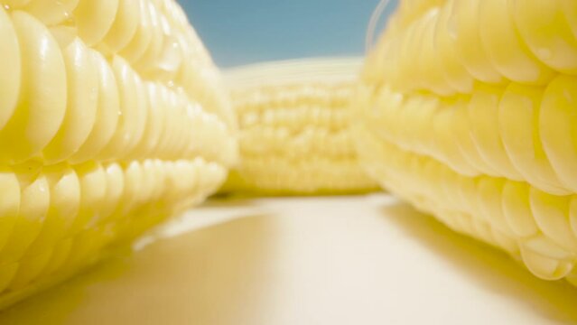 A few cobs of juicy maize are on the table. Against the blue sky. Dolly slider extreme close-up. Laowa Probe. Slow mo.
