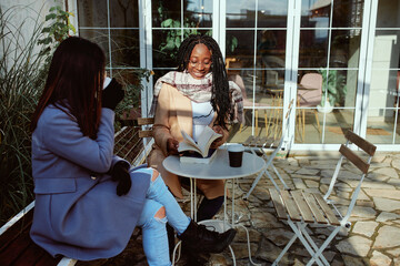 Two girls are sitting in a balcony of coffee shop, drinking coffee and talking about books.