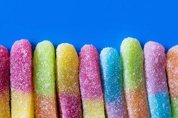 Close up view of gummy sweets with sugar on blue background.