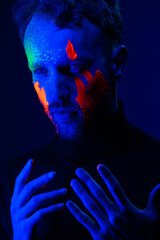 Fashion portrait. A man with fluorescent paint on his face under neon light.