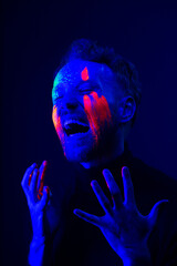 Fashion portrait. A man with fluorescent paint on his face under neon light.