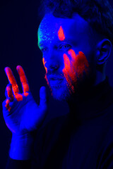 Fashion portrait. A man with fluorescent paint on his face under neon light.