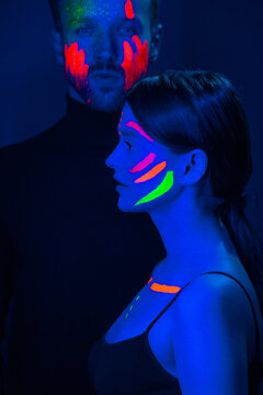 Man and woman model with fluorescent paint on face posing under ultraviolet light.