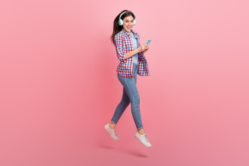 Full length photo of positive good mood lady in wireless headset surfing in telephone isolated on pink color background