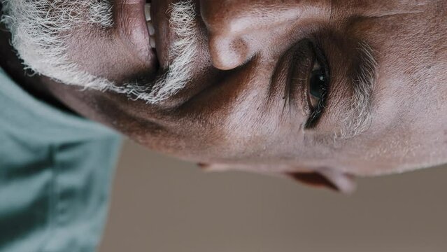 Extreme close up half face vertical view smiling old wrinkled male with gray beard bald African American man looking at camera grandpa with white smile teeth has sight eyesight problem ophthalmology