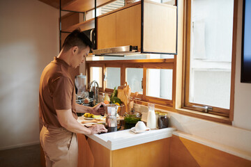 Young man turning on stove when putting moka pot on it to make morning coffee
