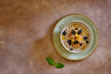 Buckwheat porridge with walnut, raisins and prunes on a green plate on a brown background under...