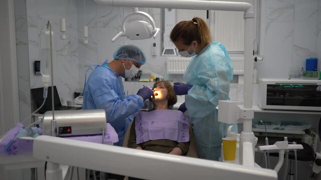 The dentist surgeon performs an implant placement operation to senior woman
