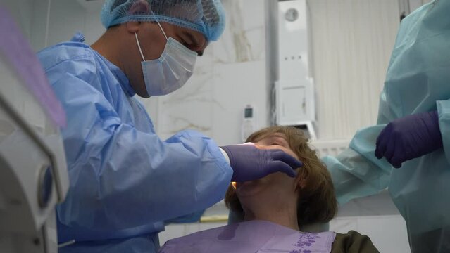 The dentist surgeon performs an implant placement operation to senior woman