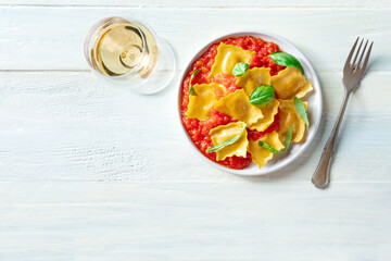 A plate of ravioli with tomato sauce and fresh basil leaves on a plate, Italian dinner, shot from the top on a rustic wooden background