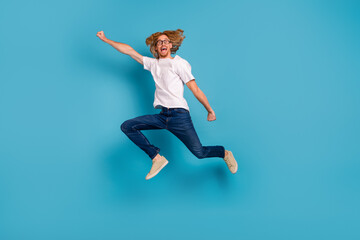 Fototapeta na wymiar Full length portrait of overjoyed sporty man raise hand flight jump isolated on blue color background