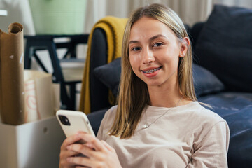 portrait of teenager girl with teeth brace using mobile phone and looking at camera