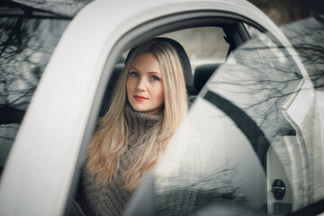 Art work. A photo of a beautiful stylish girl sitting in a car. There are beautiful reflections on the windows of the car.