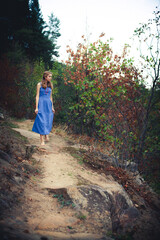 Obraz premium A positive beautiful young girl in a blue dress is resting in the mountains around beautiful nature, picturesque stones and trees.