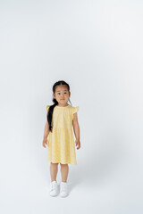 full length of asian preschooler girl in yellow dress standing on grey.