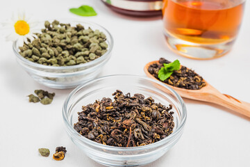 Premium black or red tea golden spirals from China, Chinese oolong tea with ginseng, brewed tea in cup. Assortment of tea in shop. White background, glass teapot.