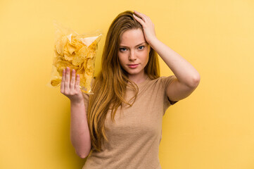 Young caucasian woman holding a bag of chips isolated on yellow background being shocked, she has...