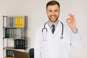 Happy doctor with stethoscope shows okay at work in clinic