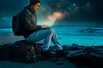 person sitting with laptop on the beach outdoors working under the starry night and milky way.