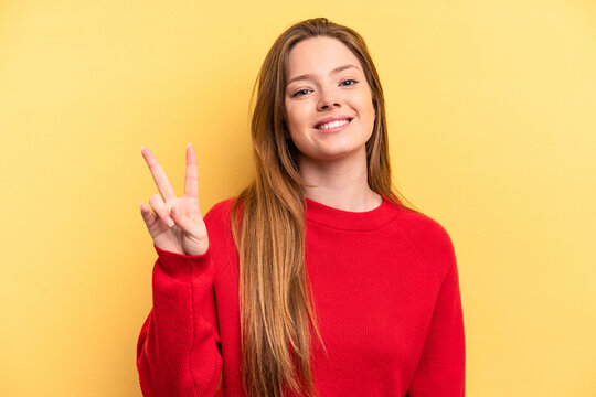 Young caucasian woman isolated on yellow background showing victory sign and smiling broadly.