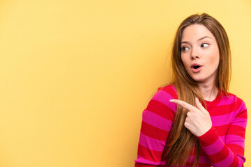 Young caucasian woman isolated on yellow background points with thumb finger away, laughing and carefree.