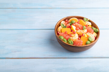Vegetarian fruit salad of pumpkin, tangerine, pomegranate, microgreen sprouts on blue, side view, copy space.