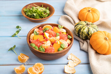 Vegetarian fruit salad of pumpkin, tangerine, pomegranate, microgreen sprouts on blue, side view, close up.
