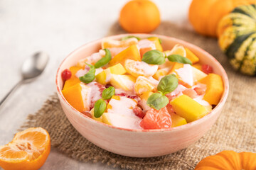 Vegetarian fruit salad of yogurt pumpkin, tangerine, basil microgreen on gray, side view, selective focus.