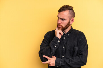 Young caucasian man isolated on yellow background looking sideways with doubtful and skeptical expression.