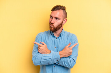 Young caucasian man isolated on yellow background points sideways, is trying to choose between two options.