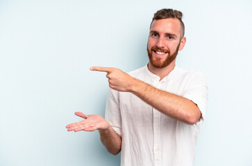 Young caucasian man isolated on blue background excited holding a copy space on palm.