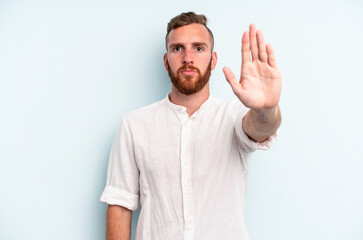 Young caucasian man isolated on blue background standing with outstretched hand showing stop sign, preventing you.