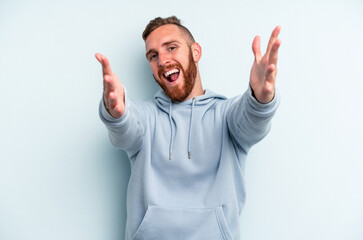 Young caucasian man isolated on blue background feels confident giving a hug to the camera.