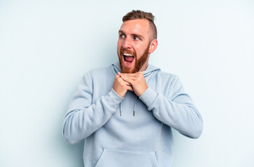 Young caucasian man isolated on blue background keeps hands under chin, is looking happily aside.