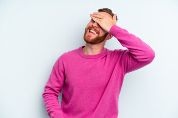 Young caucasian man isolated on blue background laughs joyfully keeping hands on head. Happiness concept.