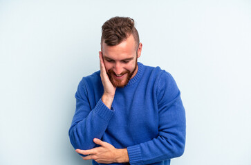 Young caucasian man isolated on blue background laughs happily and has fun keeping hands on stomach.