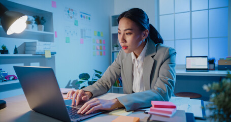 Young Asia cheerful professional businesswoman sitting on desk with laptop computer work online...