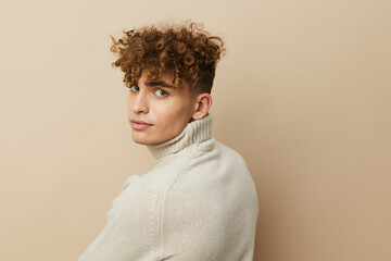 a handsome, attractive man stands on a beige background in stylish clothes and turns his back to face the camera