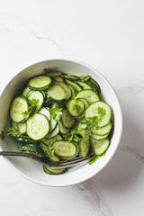 Fresh cucumber salad with cilantro and oil in white bowl.