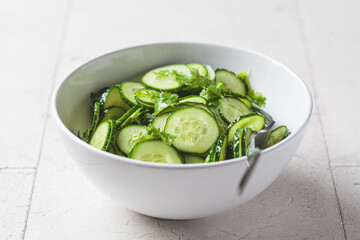 Fresh cucumber salad with cilantro and oil in white bowl.