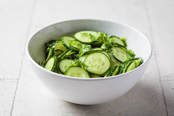 Fresh cucumber salad with cilantro and oil in white bowl.