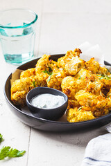 Baked spicy cauliflower with yogurt sauce in black plate. Vegan diet recipe concept.