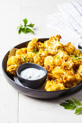 Baked spicy cauliflower with yogurt sauce in black plate. Vegan diet recipe concept.