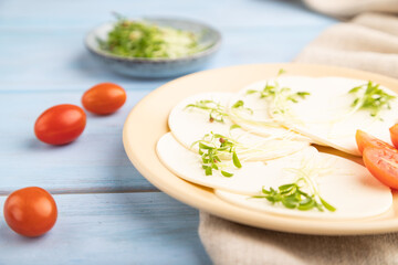 White cheese with tomatoes and cilantro microgreen on blue. side view, selective focus.