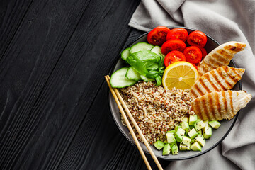 quinoa salad with grilled chicken and vegetables on a black wooden rustic background